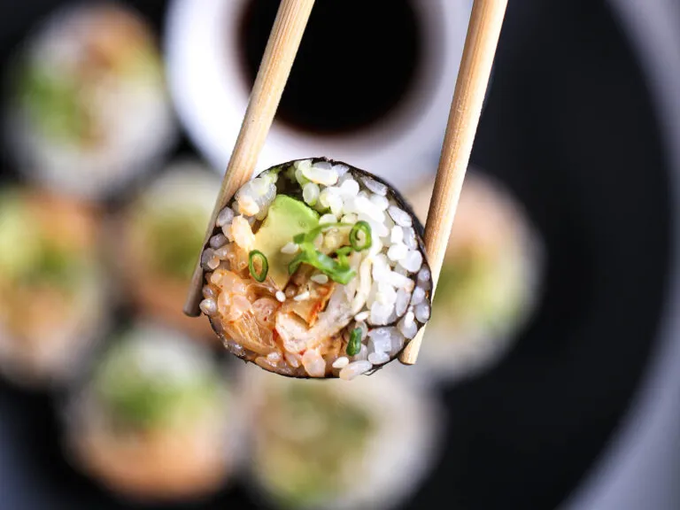 Sushi-Rolle mit Avocado und Frühlingszwiebel zwischen Stäbchen